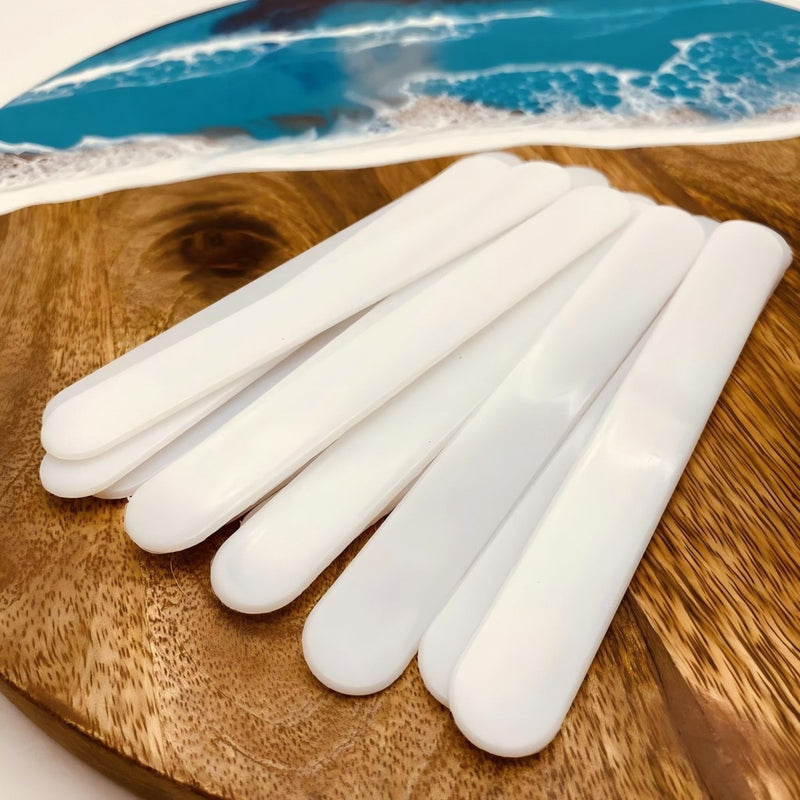 Set of 5 white silicone resin mixing sticks laid out on a wooden board